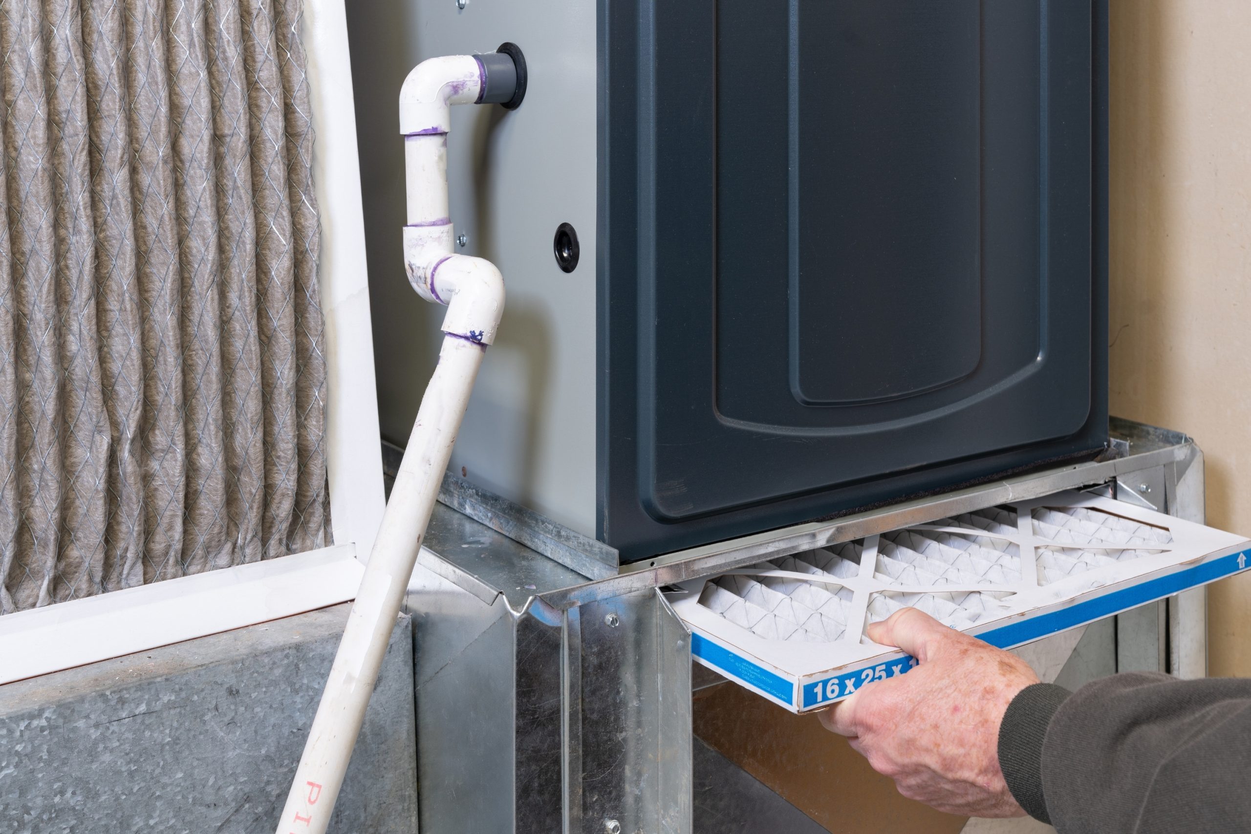 Homeowner sliding a clean pleated filter into a furnace cabinet