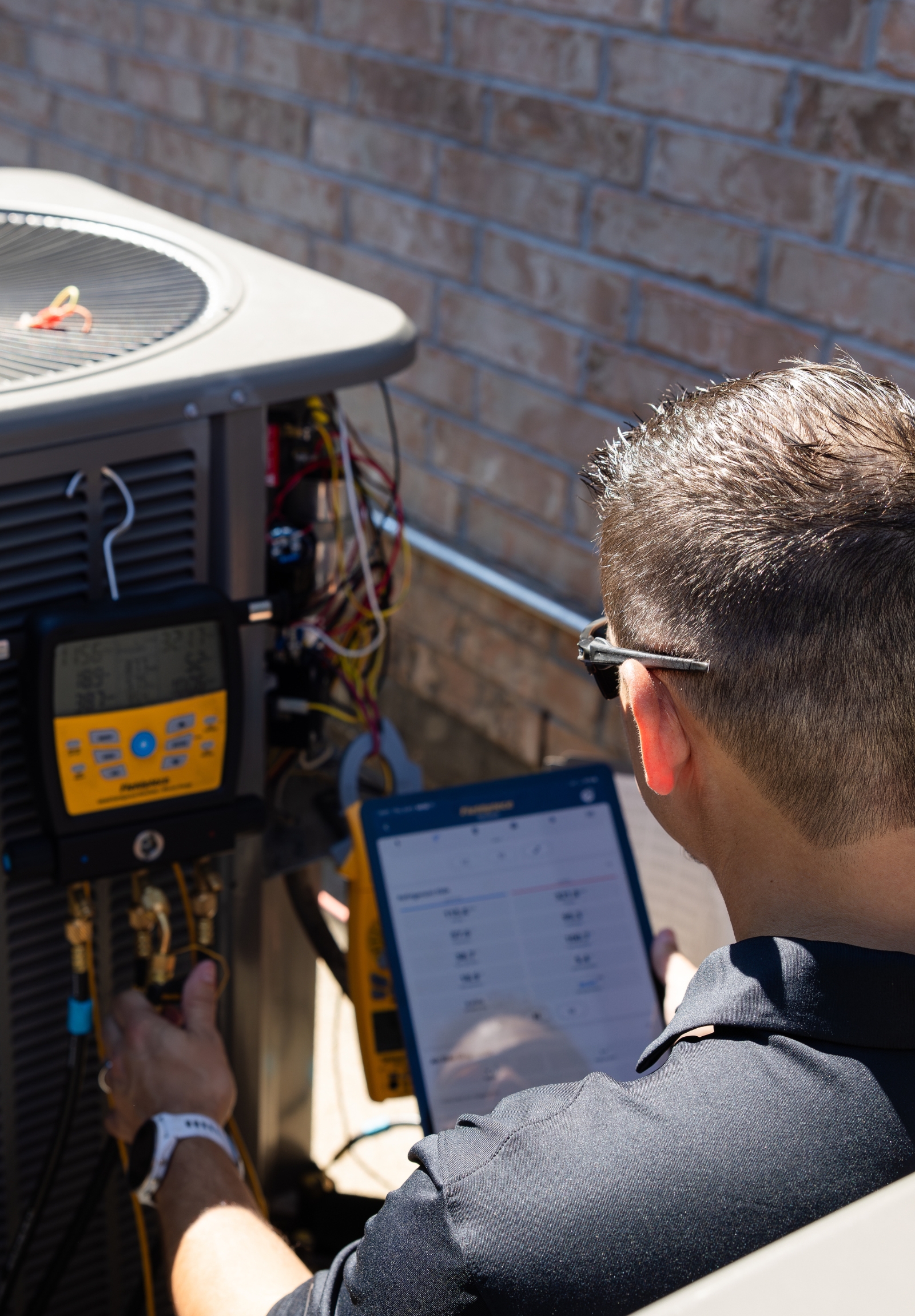 HVAC technician checking system readings on a tablet while servicing a condenser