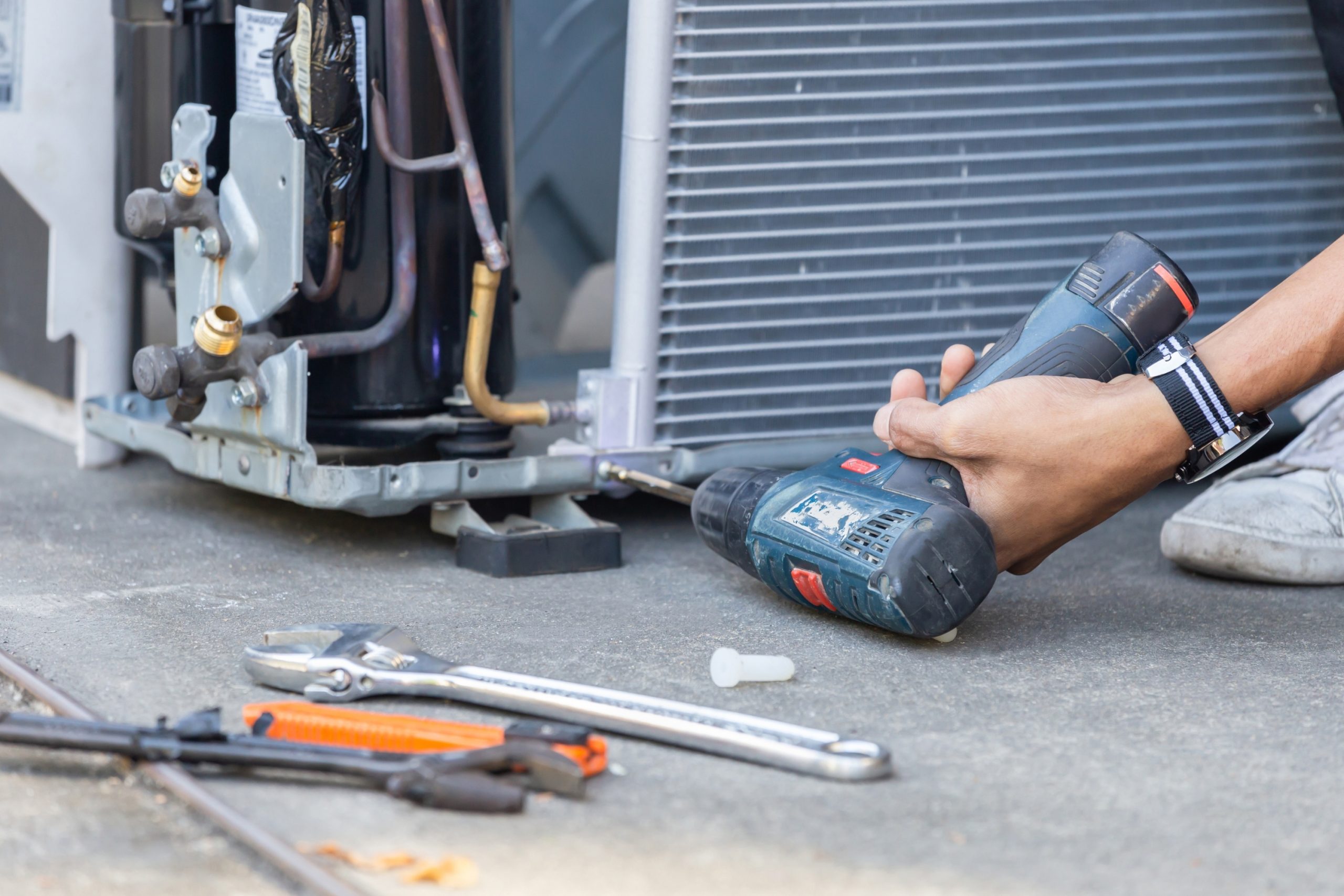 Technician using a cordless drill to open an outdoor AC condenser panel